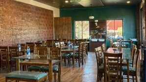 A restaurant with wooden tables and chairs, brick walls, and a green accent wall. - Art of Greens Hotel (Mahabaleshwar)