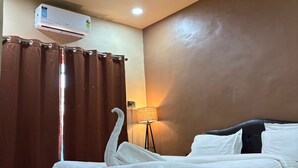 A hotel room with a bed, a standing lamp, and an air conditioning unit. - Art of Greens Hotel (Mahabaleshwar)