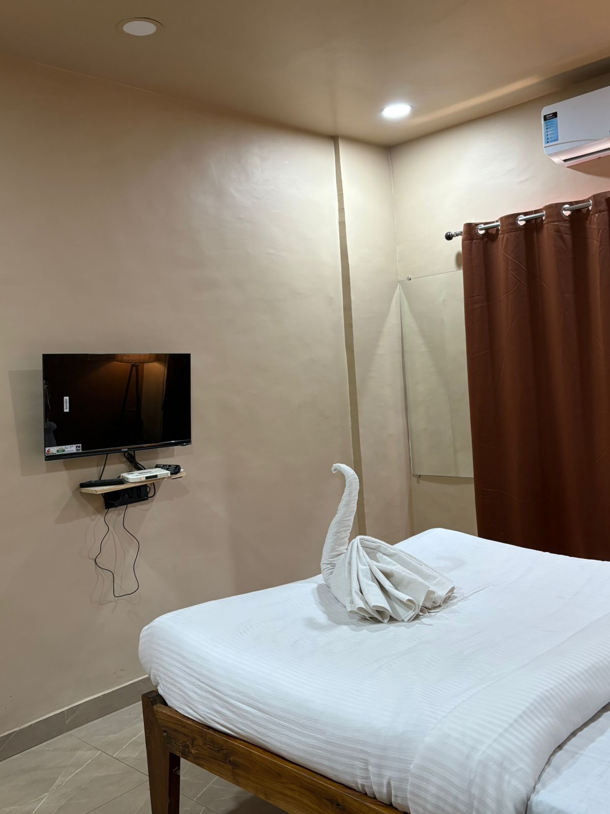 Une chambre d’hôtel équipée d’un lit, d’un téléviseur posé sur un meuble, d’un rideau de douche et d’un climatiseur fixé au mur.