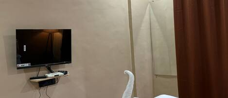 Une chambre d’hôtel équipée d’un lit, d’un téléviseur posé sur un meuble, d’un rideau de douche et d’un climatiseur fixé au mur.