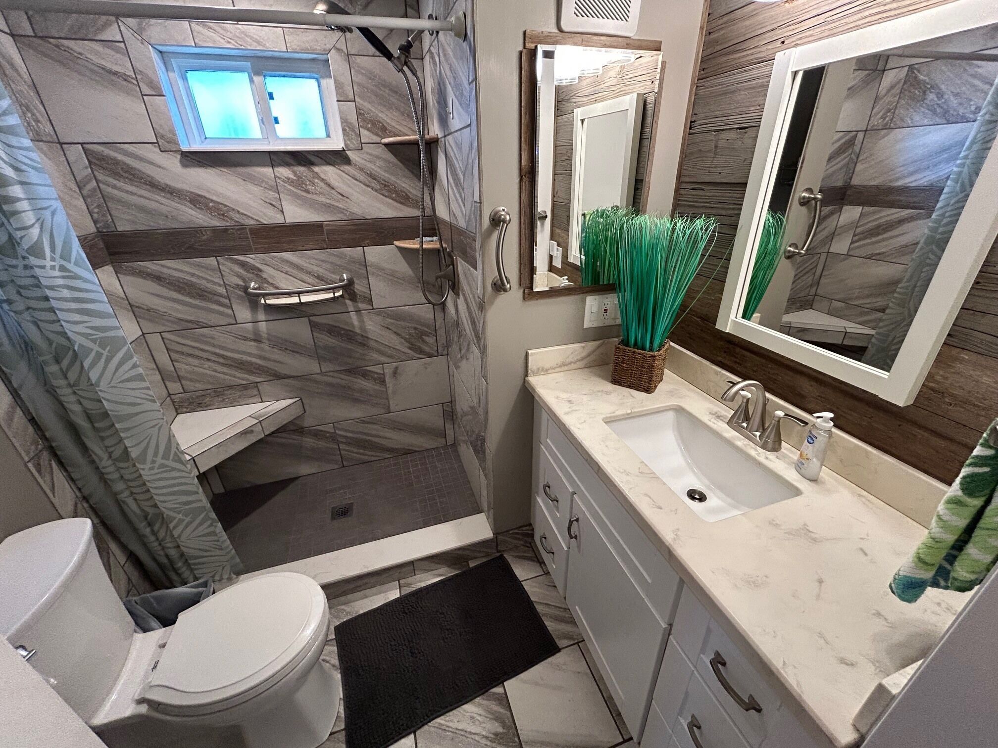 Un baño con inodoro, ducha, lavamanos y espejo.