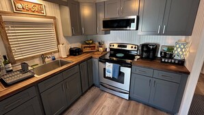 A compact kitchen with grey cabinets, a stainless steel sink, a microwave, a stove, and a coffee maker. - Bridge Street Beach House | Wi-Fi | Center of All (Bradenton Beach)