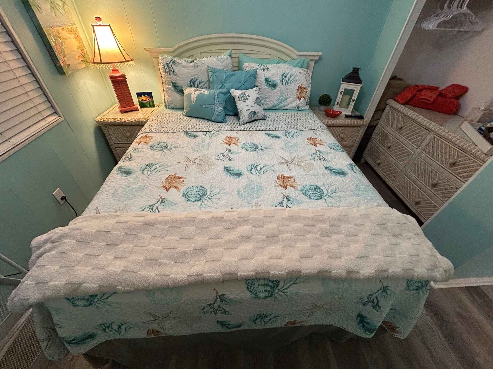 A bed with a floral quilt, a nightstand with a lamp, and a dresser with red towels.