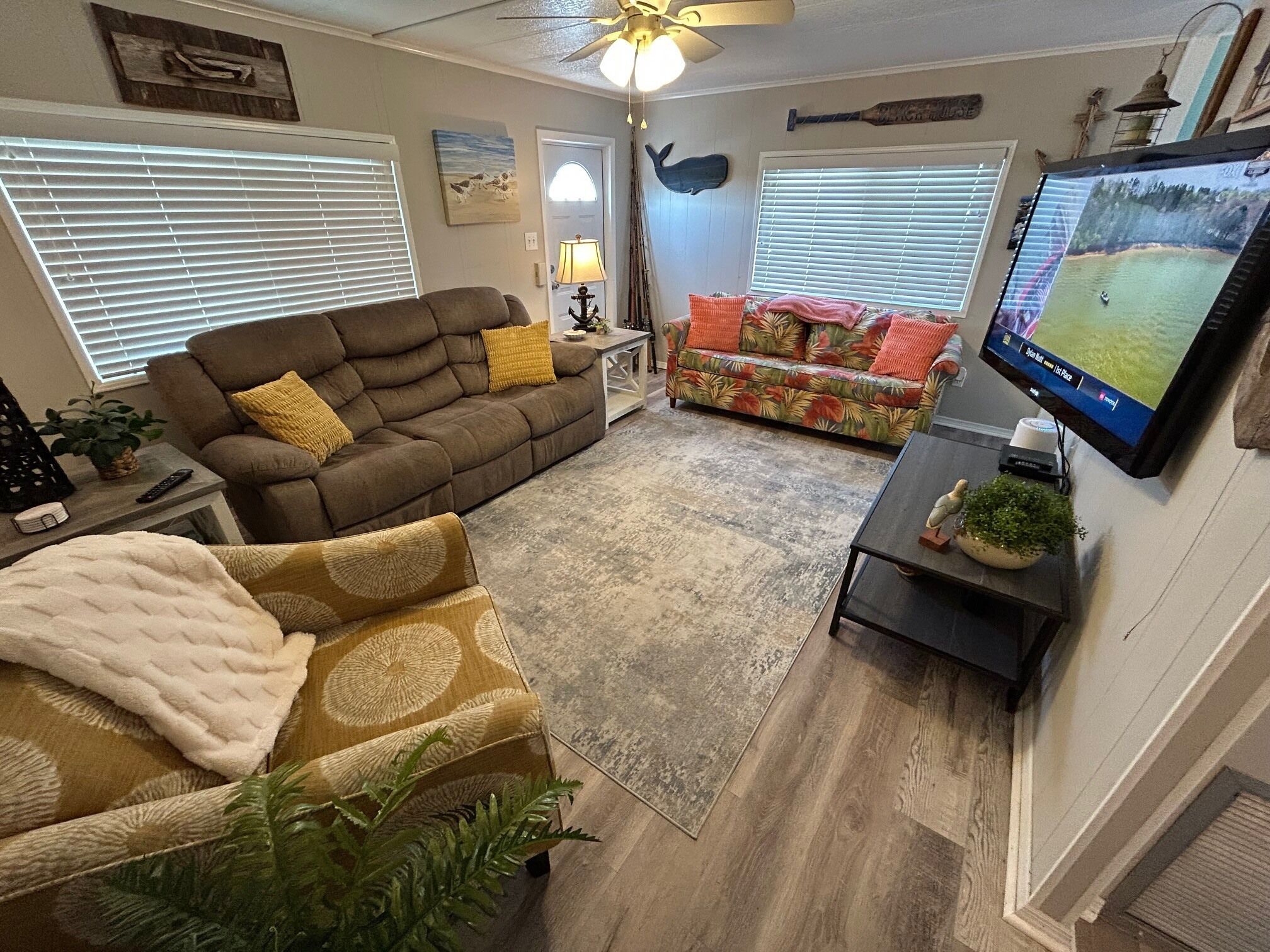 A living room with a brown sofa, a colorful sofa, a TV, and a ceiling fan.