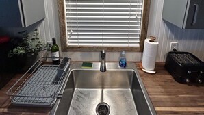 A kitchen with a stainless steel sink, a wooden countertop, a window with blinds, and a sign above the window. - Bridge Street Beach House | Wi-Fi | Center of All (Bradenton Beach)
