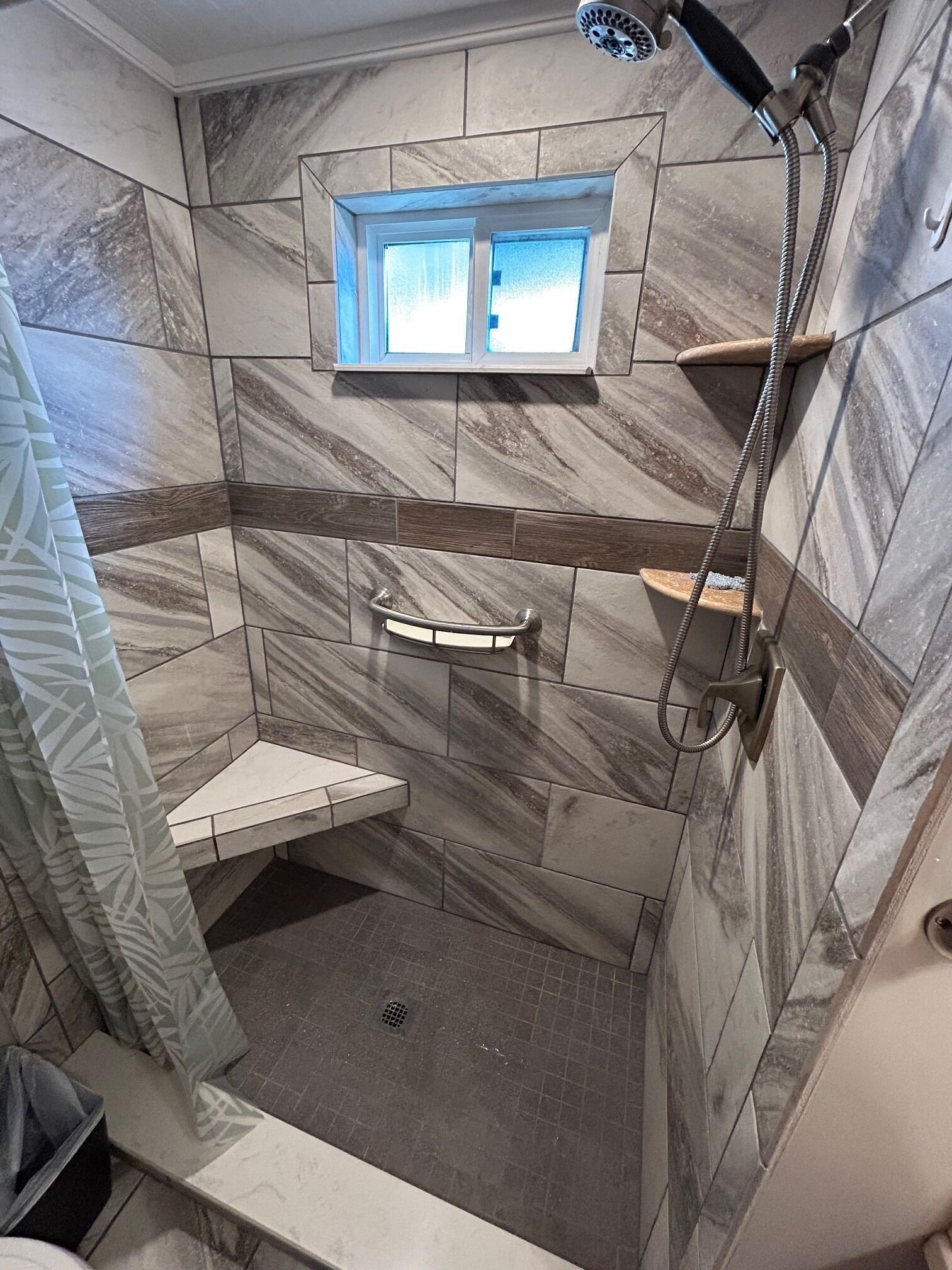 A shower with a handheld showerhead, a window above the shower, and a towel rack.