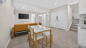 A modern apartment with a dining area, a sofa, a TV, and a staircase. - 2 Bed | Mins to Airport | Modern Suite (Calgary)