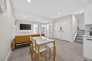 Um apartamento moderno com área de jantar, sofá, televisão e escada.