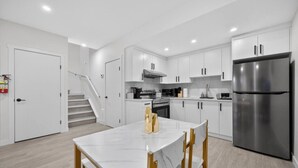 A modern kitchen with white cabinets, a stainless steel refrigerator, and a marble countertop. - 2 Bed | Mins to Airport | Modern Suite (Calgary)
