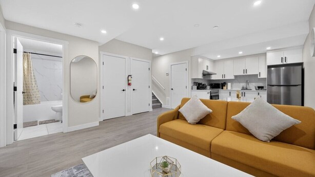 A modern living room with a sofa, a coffee table, and a kitchen in the background. - 2 Bed | Mins to Airport | Modern Suite (Calgary)