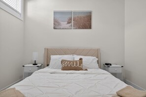 Quarto com cama, duas mesas de cabeceira, um criado-mudo, luminária na parede e duas molduras com imagens.