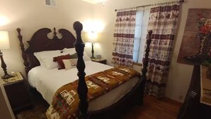 A four-poster bed with a patterned bedspread, a nightstand with a lamp, and a window with patterned curtains.