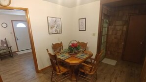 A dining area with a wooden table and chairs, a clock on the wall, and framed pictures.