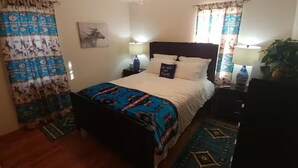 A bedroom with a bed, bedside lamps, a nightstand, a dresser, and a window with curtains.