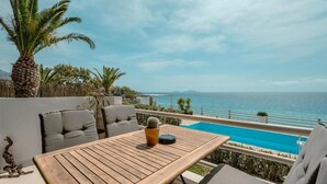A wooden table with a potted cactus, grey cushioned chairs, a small pool, and a view of the sea and mountains. - East of Preveli Villas (Agios Vasileios)