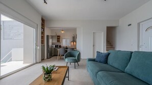 A modern living room with a sofa, a coffee table, and a chair. There is a kitchen in the background with cabinets and a dining area. - East of Preveli Villas (Agios Vasileios)