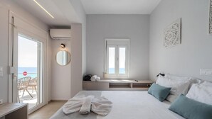 A bedroom with a bed, a bench, a window, and a view of the sea. - East of Preveli Villas (Agios Vasileios)