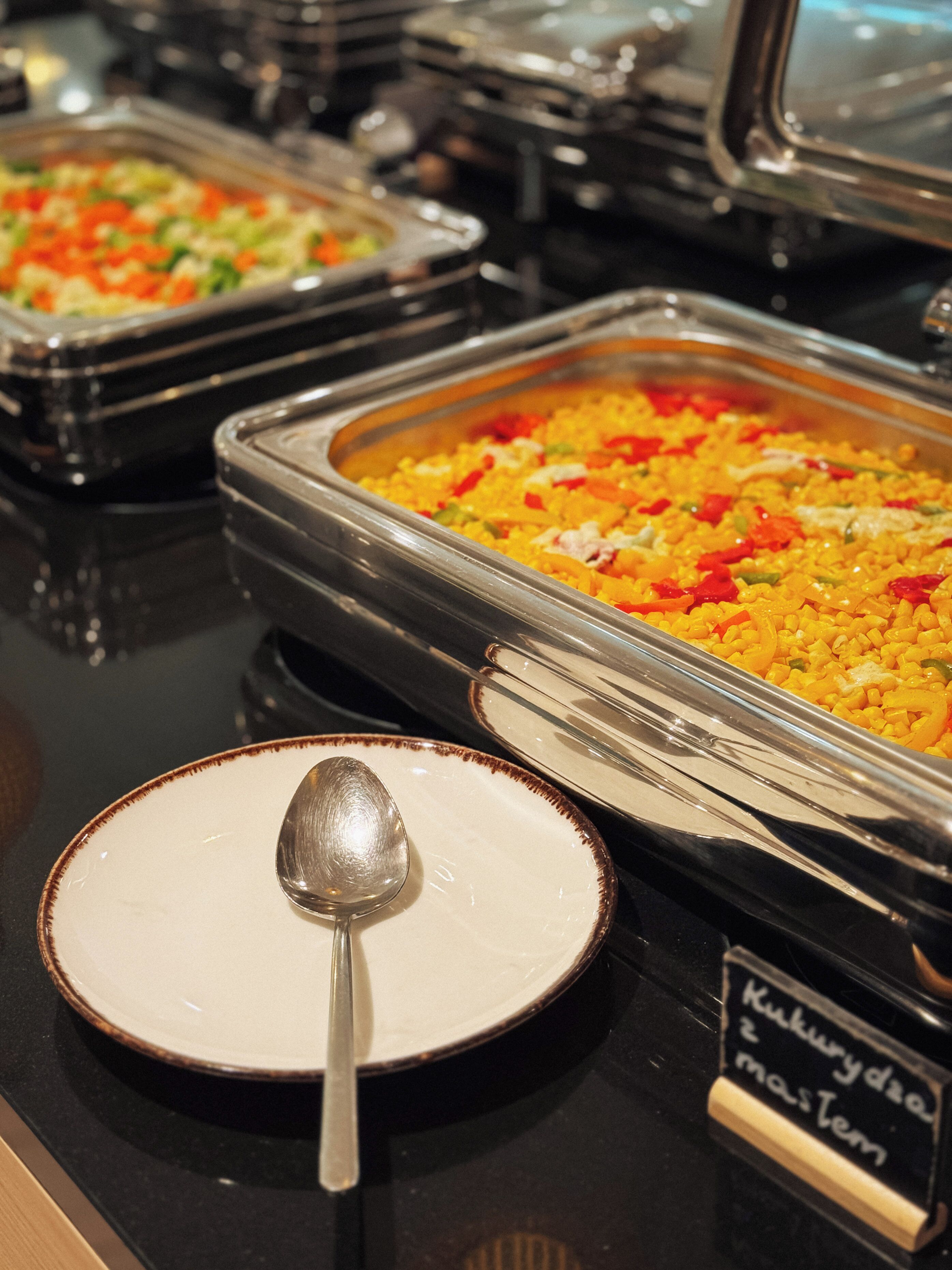 A buffet with various dishes, a spoon on a plate, and a sign with text.