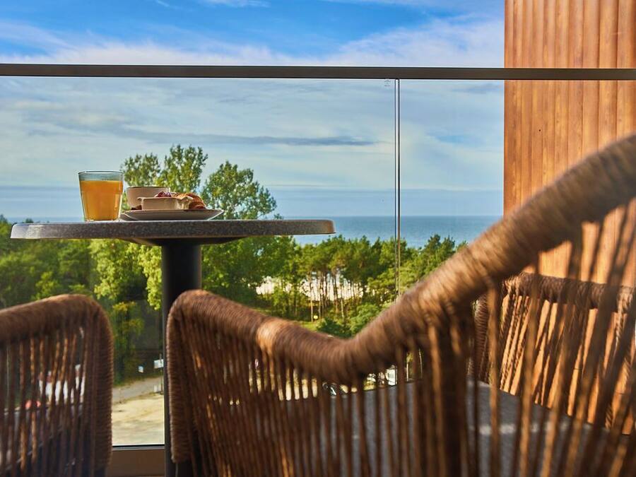 A balcony with wicker chairs, a table with a glass of orange juice, and a view of the sea.