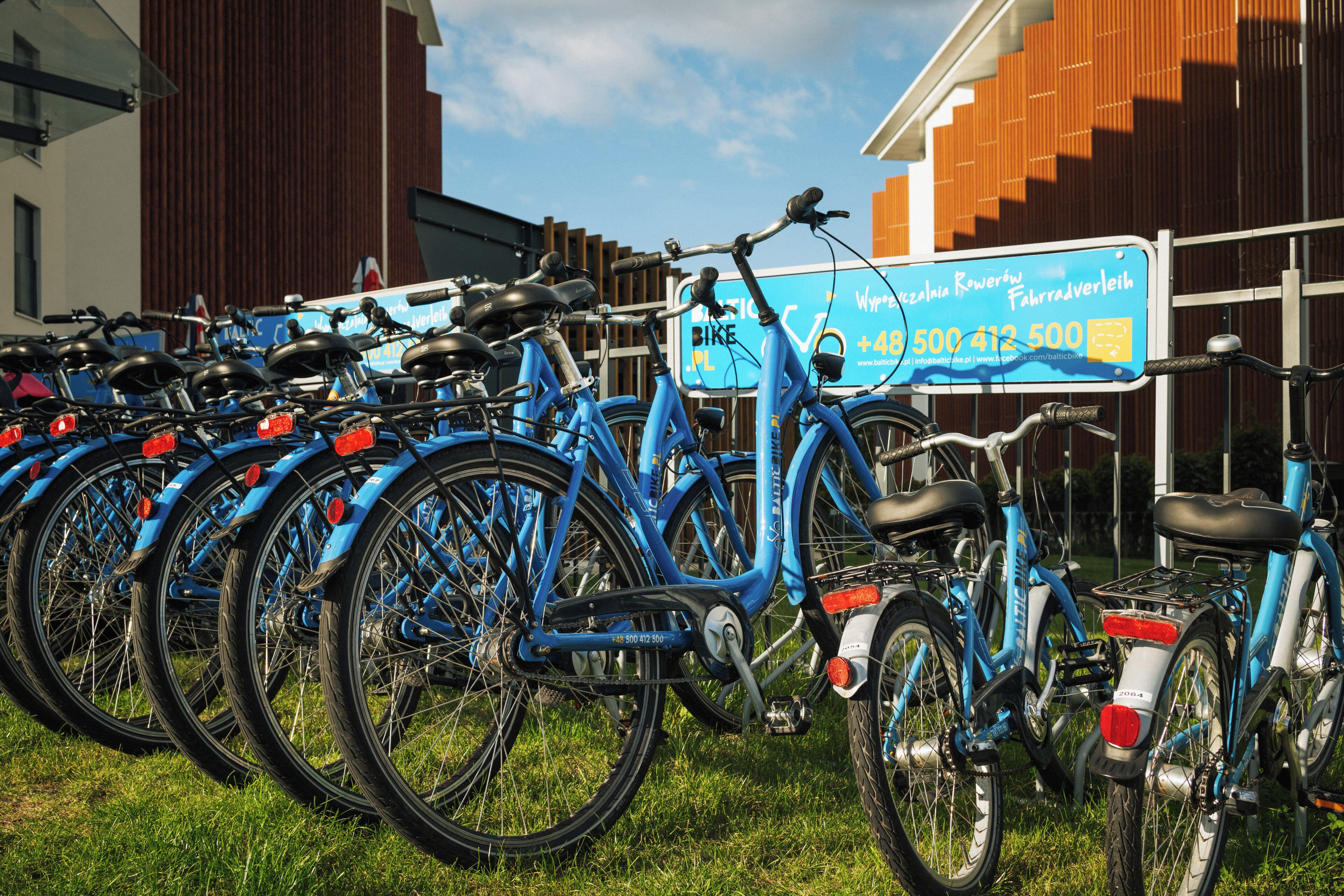 A row of blue bicycles parked on grass in front of a building with a sign.