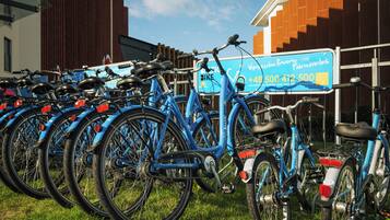 A row of blue bicycles parked on grass in front of a building with a sign.