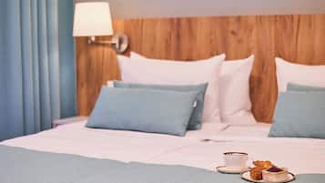 Une chambre d’hôtel avec une tête de lit en bois, un lit avec une literie bleue et blanche, une lampe de chevet et un plateau de petit-déjeuner avec des croissants et une tasse.