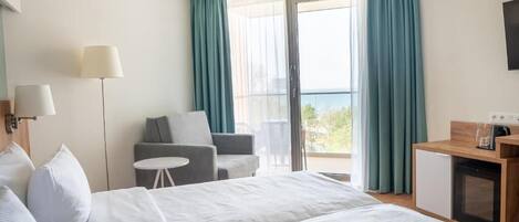 A hotel room with a bed, a small table, a chair, a desk, and a TV.