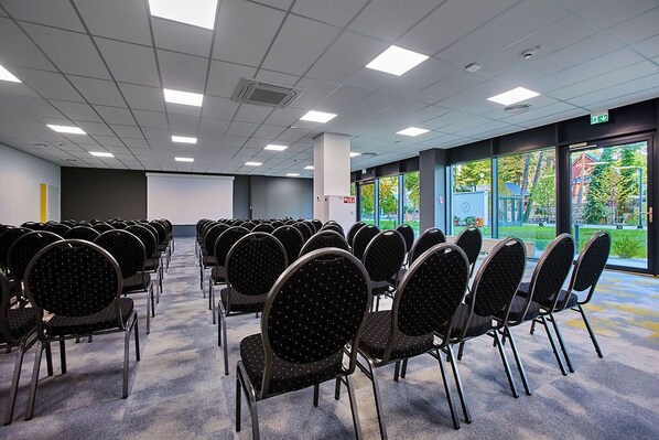 A conference room with rows of chairs, a projector screen, and large windows with a view of greenery.