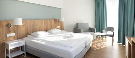 Een hotelkamer met een groot bed, twee nachtkastjes, een bureau, een stoel en een raam met gordijnen.