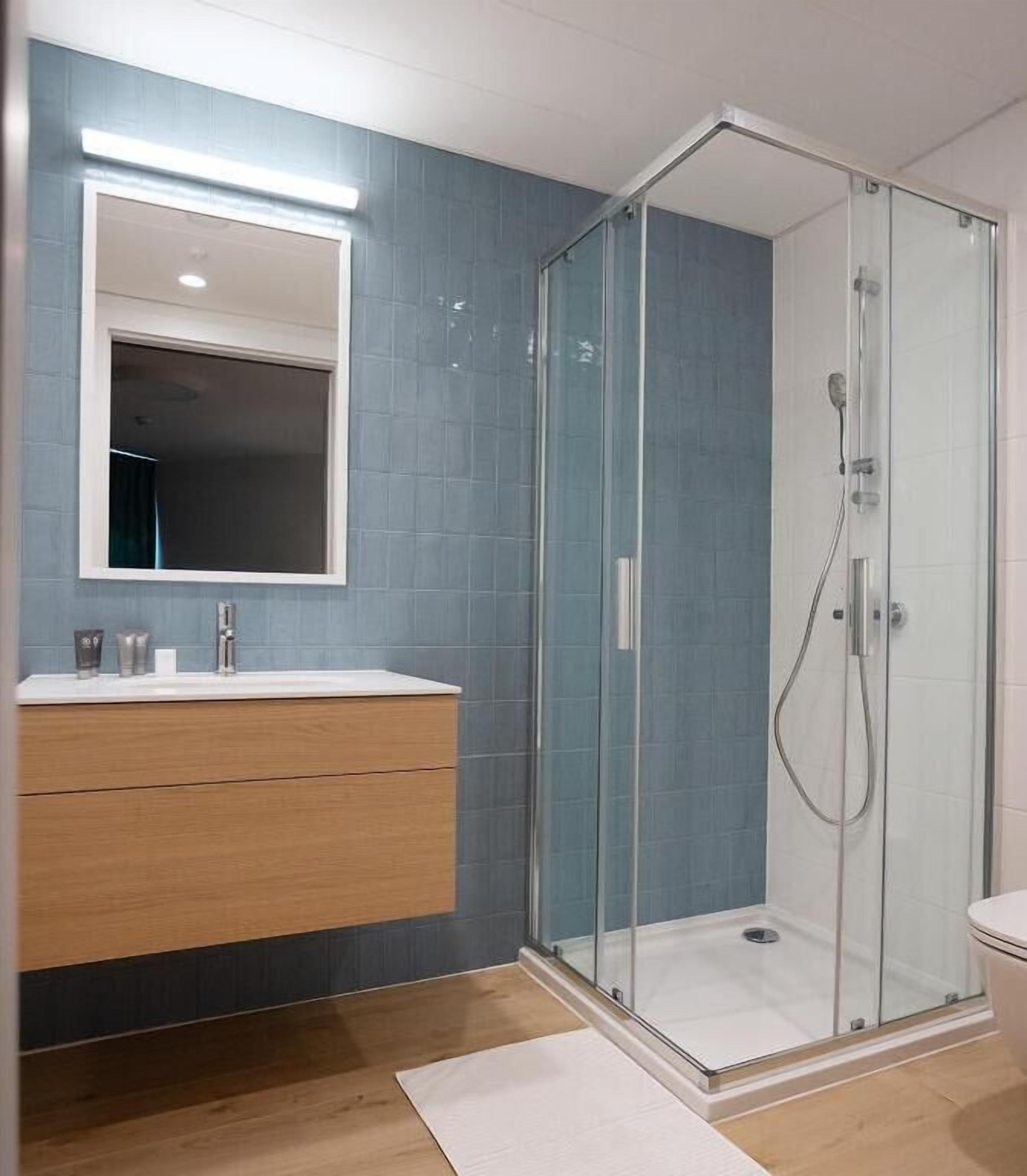 A modern bathroom with a glass-enclosed shower, a wooden vanity, and a large mirror.
