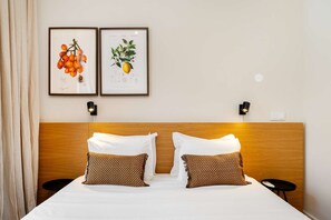Ein Hotelzimmer mit einem hölzernen Kopfteil, zwei gerahmten Pflanzenbildern, zwei Nachttischlampen und zwei gemusterten Kissen.