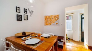 Comedor con mesa de madera, sillas blancas, una piña, croissants y un vaso de jugo de naranja.
