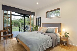 Ein Schlafzimmer mit einem Bett, Nachttischen, einem Sessel, einem Fenster und Blick ins Freie.
