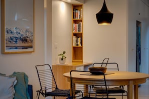 Ein Essbereich mit einem runden Tisch, Metallstühlen, einem Bücherregal, einer Pendelleuchte und einem gerahmten Bild an der Wand.