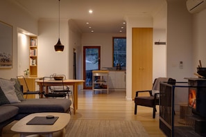 Ein gemütliches Wohnzimmer mit einer Couch, Couchtisch und Kamin. Es gibt einen Essbereich mit Tisch und Stühlen, und im Hintergrund eine Küche.