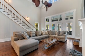 A spacious living room with a large sectional sofa, a wooden coffee table, and a staircase with a ceiling fan. - 5 BR 4 BA Home Close To The Marsh Walk (Murrells Inlet)