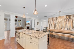 A spacious kitchen with a marble island, wooden dining table, and pendant lighting. - 5 BR 4 BA Home Close To The Marsh Walk (Murrells Inlet)
