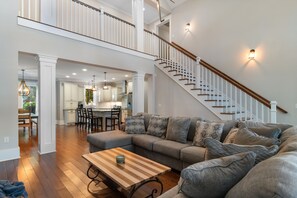 A spacious living area with a large sectional sofa, a wooden coffee table, and a staircase with a railing. - 5 BR 4 BA Home Close To The Marsh Walk (Murrells Inlet)