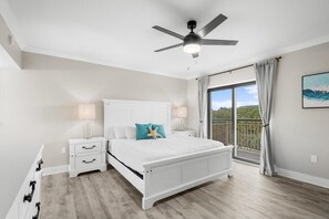 A bedroom with a white bed, two bedside tables, a ceiling fan, and a large window with a view. - Beach Time Oceanview 3 Bedroom (Pawleys Island)