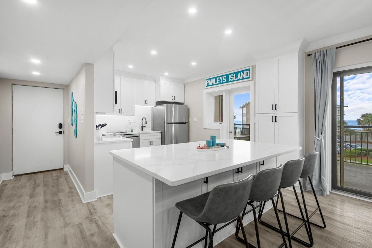 A modern kitchen with white cabinetry, a stainless steel refrigerator, and a bar area with grey stools.