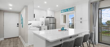 A modern kitchen with white cabinetry, a stainless steel refrigerator, and a bar area with grey stools.