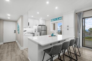 A modern kitchen with white cabinetry, a stainless steel refrigerator, and a bar area with grey stools. - Beach Time Oceanview 3 Bedroom (Pawleys Island)