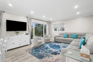 A living room with a flat-screen TV, a grey sofa with teal cushions, a white cabinet, and a patterned rug. - Beach Time Oceanview 3 Bedroom (Pawleys Island)