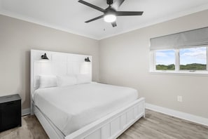 Une chambre à coucher avec un lit, un ventilateur de plafond, une fenêtre donnant sur un beau paysage et une table de chevet.
