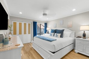 Ein Schlafzimmer mit Bett, Nachttischen, einem Schminktisch, einem Fenster mit Vorhängen und einem Deckenventilator.