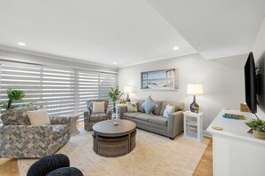 A modern living room with a sofa, armchair, coffee table, and a flat-screen TV mounted on the wall. - 3 Bedroom Vacation Condo near the Beach (Pawleys Island)