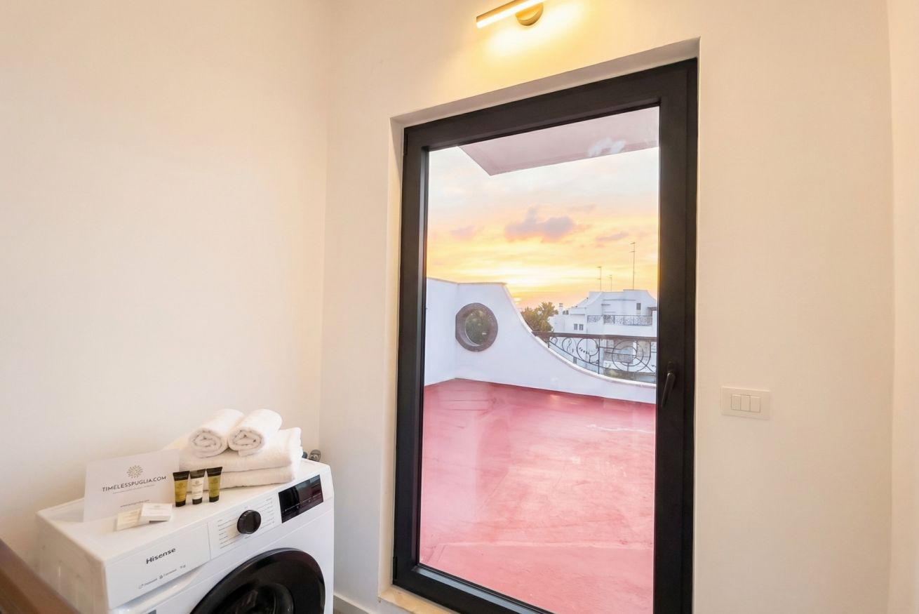 Ein Zimmer mit Waschmaschine, Handtuchhalter mit Handtüchern und Blick auf einen Sonnenuntergang durch eine Glastür.