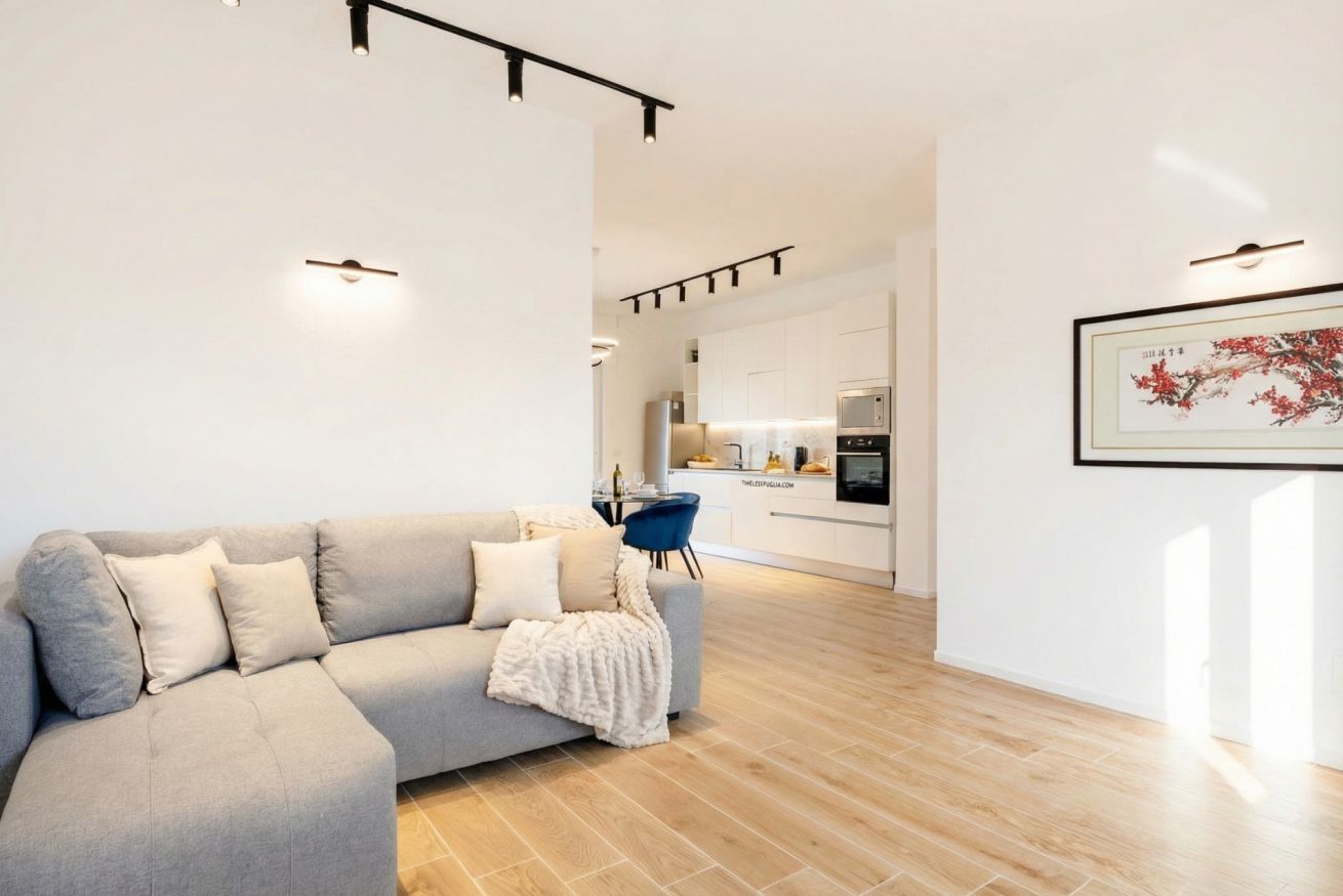 Uma sala de estar moderna com um sofá cinza, uma poltrona azul e uma cozinha ao fundo.