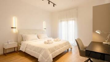 A hotel room with a bed, bedside table, desk, chair, and a window with curtains.