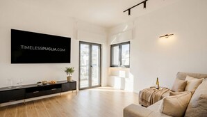 A modern living room with a flat-screen TV, a sofa, a coffee table, a plant, and a dining area with a table and chairs. - MareVista - Private Garden & Parking (Bari)